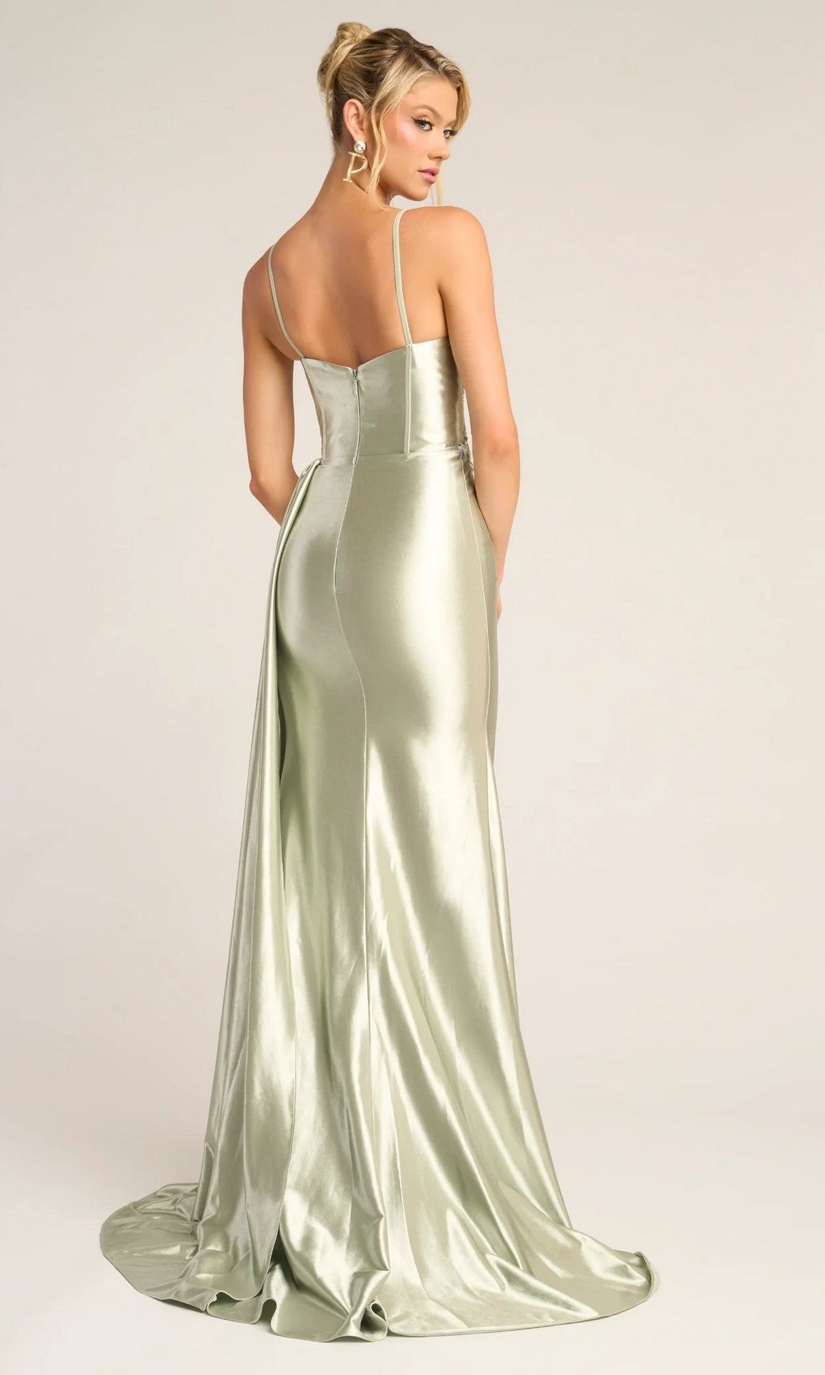 A woman stands with her back to the camera in the Portia and Scarlett PS26270 long prom dress, featuring light green satin, thin straps, a low back, and a sheer corset bodice against a plain background.